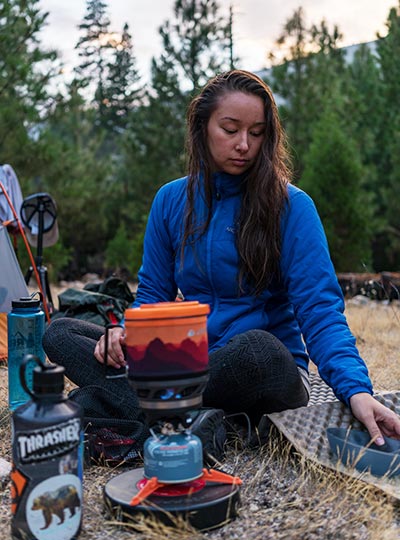 Fotografie Adély sedící v tábořišti, která připravuje jídlo na plynovém vařiči